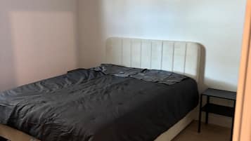 Una cama individual con cabecera blanca en una habitación con paredes de tonos claros y suelo de madera.