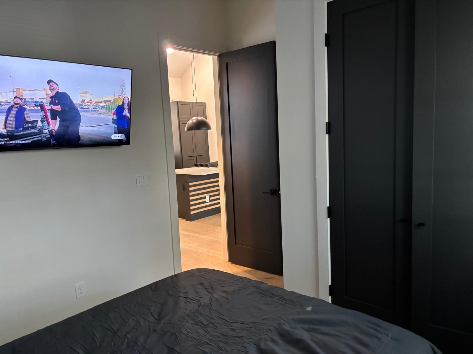 Un dormitorio con cama, televisor montado en la pared y puerta que da al baño.
