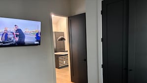 Un dormitorio con cama, televisor montado en la pared y puerta que da al baño.