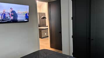 Un dormitorio con cama, televisor montado en la pared y puerta que da al baño.