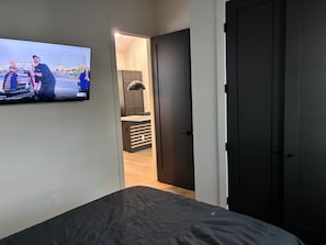 Een slaapkamer met een bed, een aan de muur bevestigde televisie en een deur naar een badkamer.