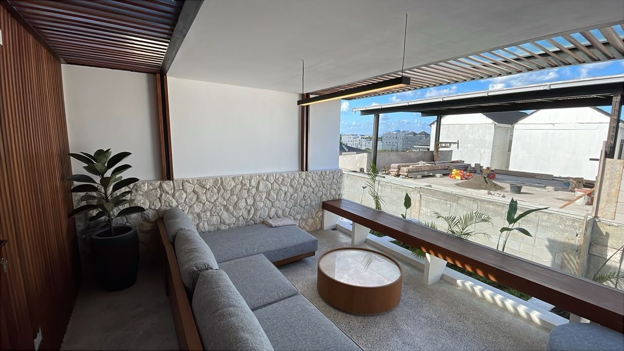 A modern living room with a stone accent wall, a grey sectional sofa, a round coffee table, and a view of construction work outside.