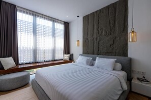 A modern bedroom with a large bed, a bench by the window, and a stone accent wall. - Pantai Lima 2BR Villa - Rooftop - 500m to Beach (Badung)