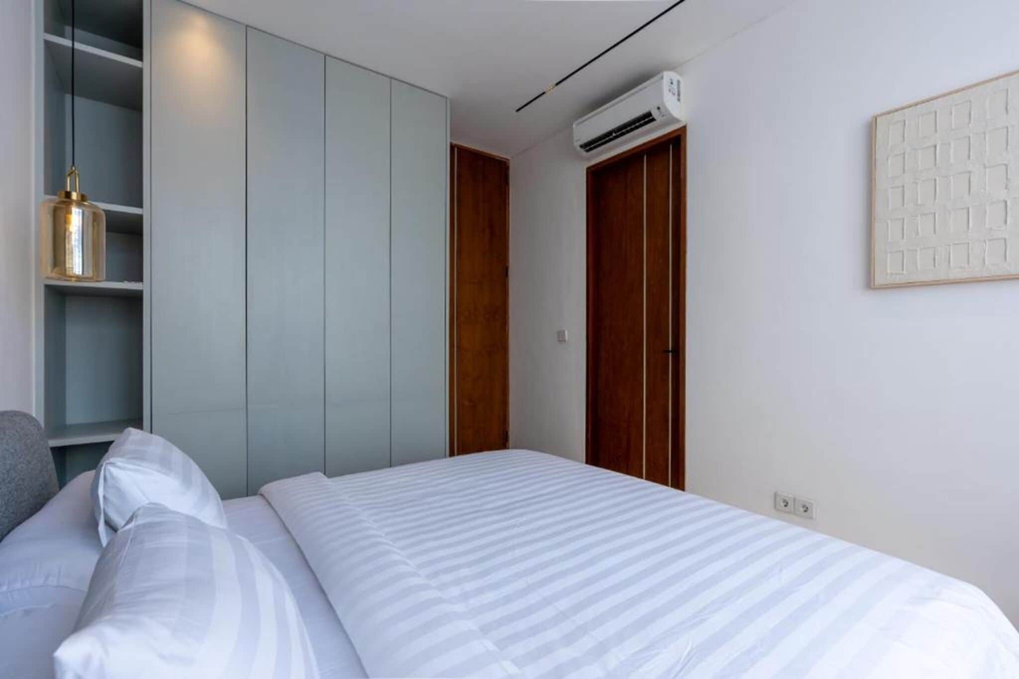 Une chambre à coucher comprenant un lit, une armoire, un appareil de climatisation et un luminaire fixé au mur.