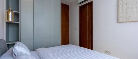 A bedroom with a bed, a wardrobe, an air conditioning unit, and a wall-mounted light fixture.