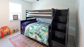 A bunk bed with a built-in desk and shelving, a window with blinds, a colorful rug, and a ceiling fan.