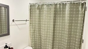 Et badeværelse med toilet, håndvask med toiletartikler, bruseforhæng og en måtte.