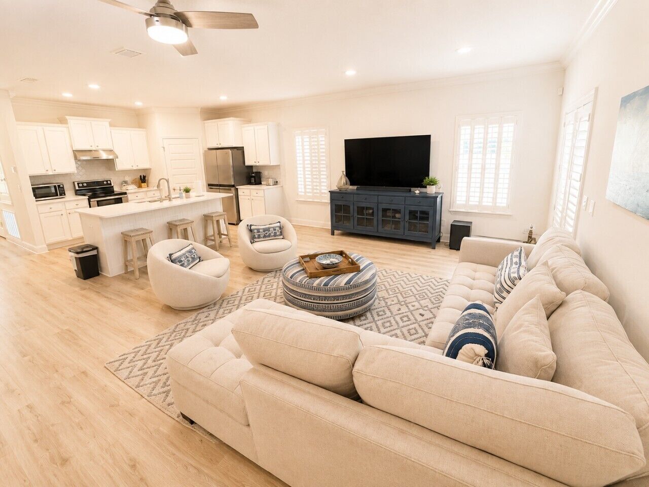A spacious living area with a sofa, ottoman, and chairs, a kitchen with modern appliances, and a flat-screen TV.