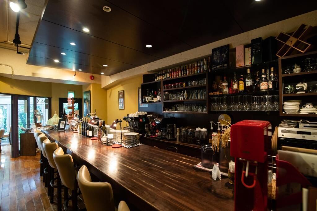 A bar area with a long counter, bar stools, and shelves stocked with bottles and glasses.