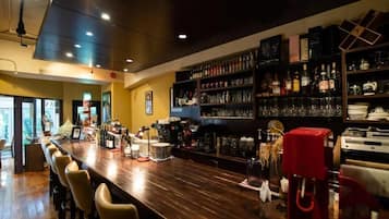 A bar area with a long counter, bar stools, and shelves stocked with bottles and glasses.