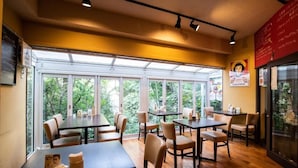 Een restaurant met meerdere tafels en stoelen, grote ramen met uitzicht op groen, en een menubord aan de muur.