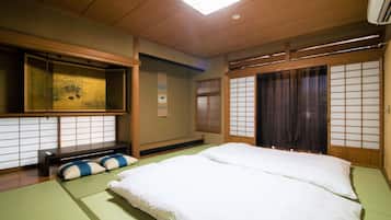 A traditional Japanese-style room with tatami flooring, a low bed with white bedding, a futon, a shoji screen, and a sliding door.