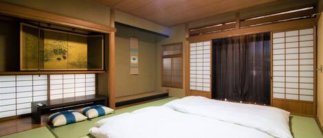 A traditional Japanese-style room with tatami flooring, a low bed with white bedding, a futon, a shoji screen, and a sliding door.