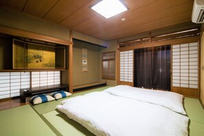 A traditional Japanese-style room with tatami flooring, a low bed with white bedding, a futon, a shoji screen, and a sliding door. - Arbor house (Kagoshima , Nishida)