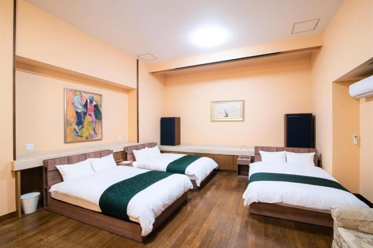 Habitación de hotel con tres camas, suelo de madera y obras de arte en las paredes.