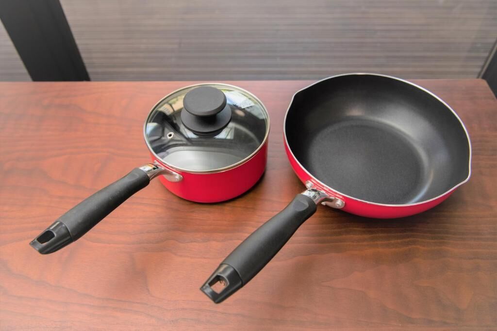 Two red cookware items with black handles on a wooden surface.