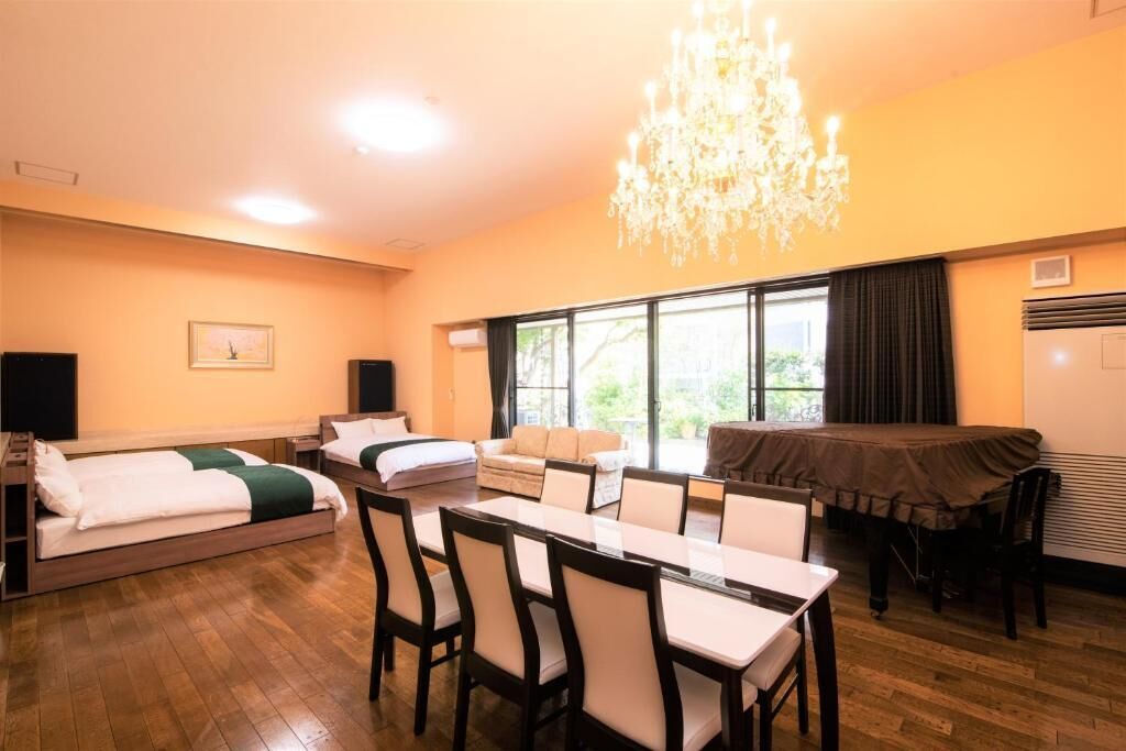 Una camera d'albergo con un tavolo da pranzo, sedie, un divano, un letto, un lampadario e ampie finestre.