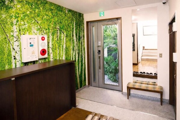A reception area with a green leafy wall, a reception desk, an elevator, and a bench.