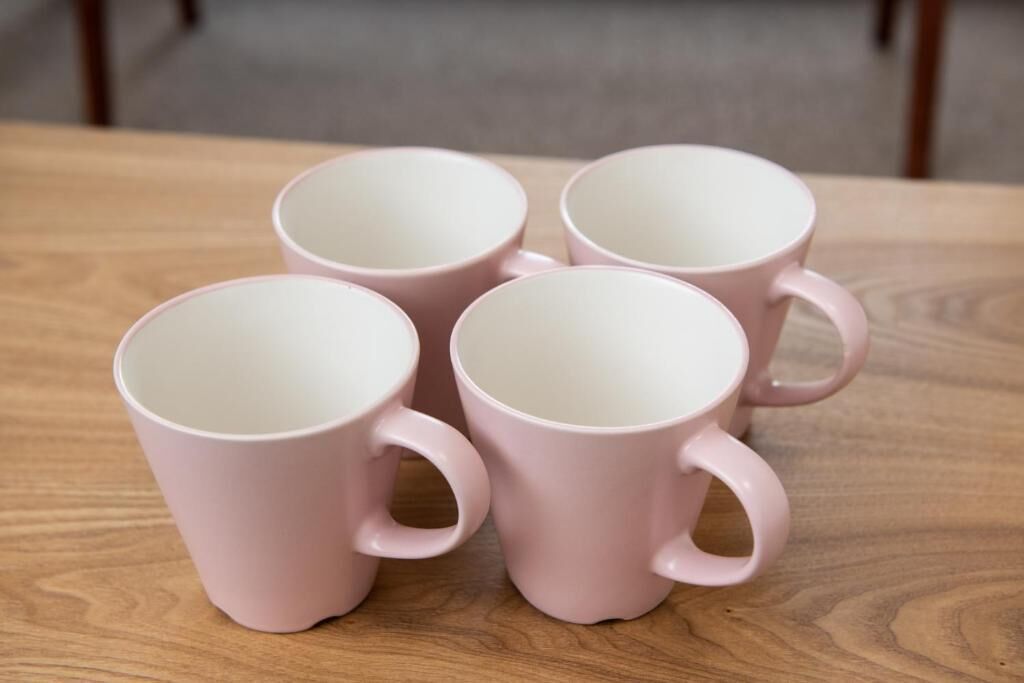 Quatre tasses en céramique rose sur une table en bois.
