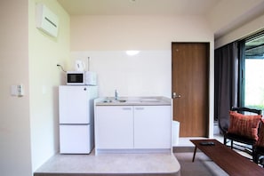 A compact kitchen with a microwave, sink, and a small table with a remote control.