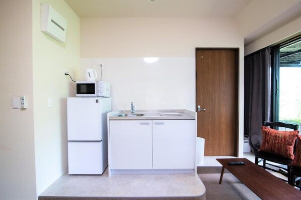 A compact kitchen with a microwave, sink, and a small table with a remote control.