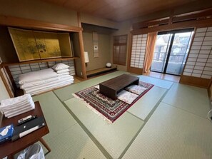 A tatami mat room with a futon bed, a small table with a remote control, and a sliding door leading to a balcony.