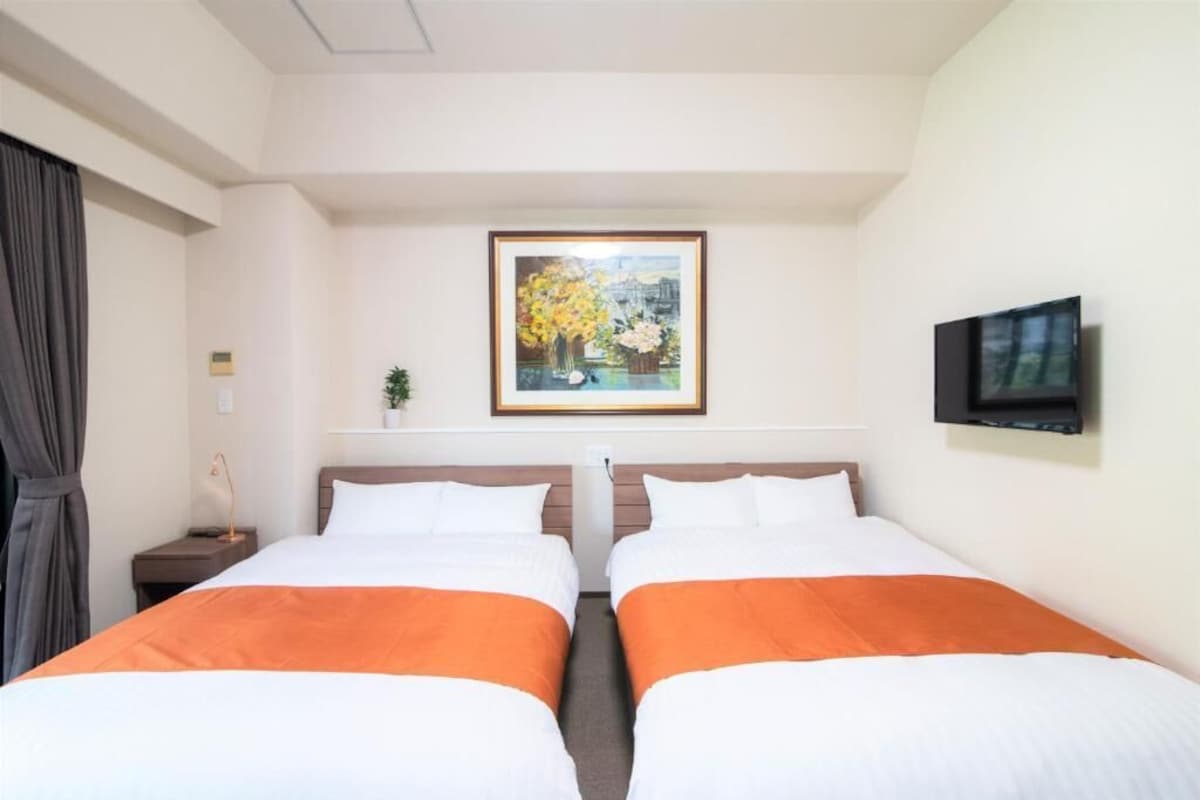 Habitación de hotel con dos camas, un cuadro en la pared, un televisor y una mesita con una lámpara.