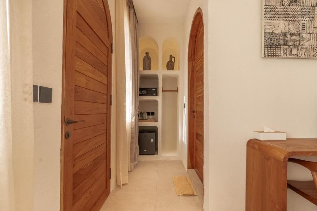 A hallway with wooden doors, a small table, and a shelf with decorative items.