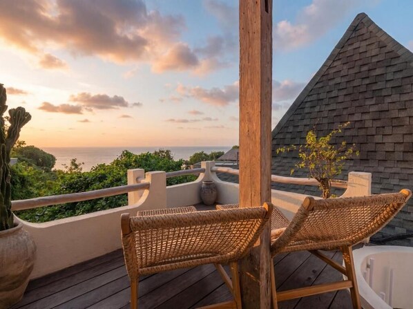 A balcony with wicker chairs, a view of the sea, and a pyramid-shaped structure.
