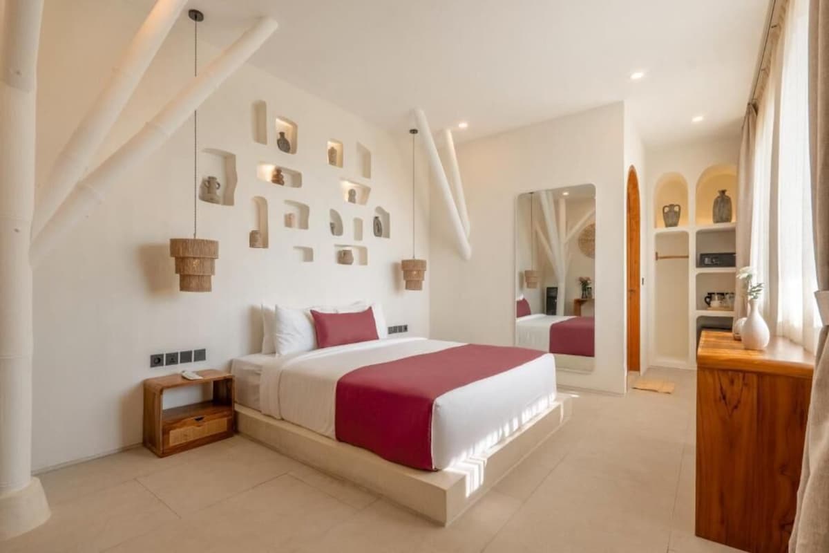 A modern bedroom with a large bed, a wooden nightstand, a mirror, and a wall with shelves.