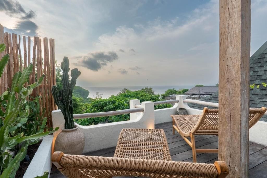 A wooden deck with wicker chairs and a cactus planter, overlooking a coastal landscape.