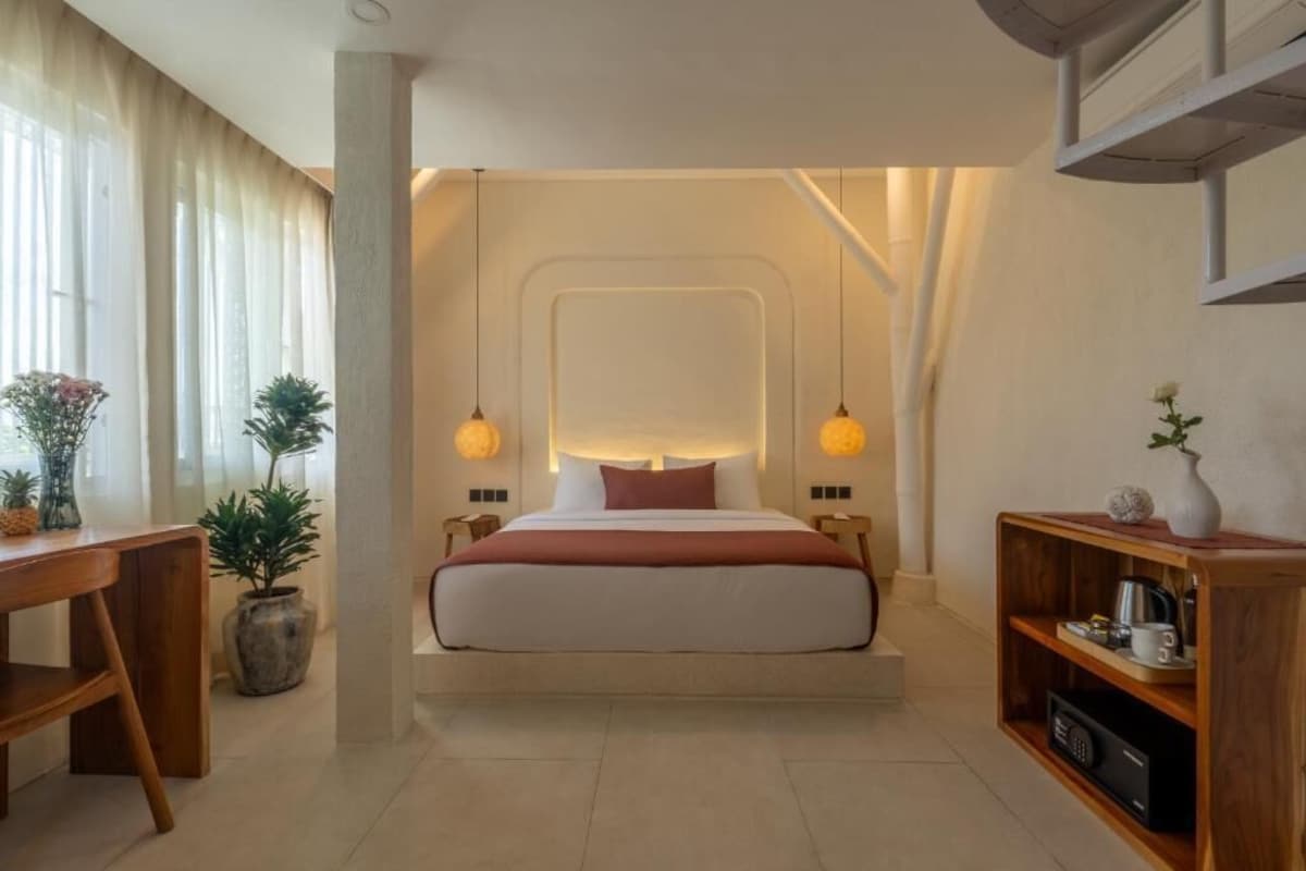 A modern hotel room with a bed centered in the space, flanked by a wooden side table and a built-in shelf with a coffee maker.