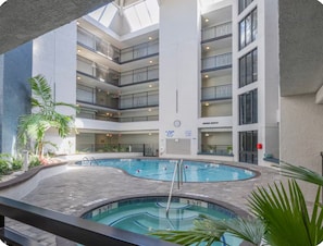 En indendørs swimmingpool med flere balkon niveauer, omgivet af planter og et ur på væggen.