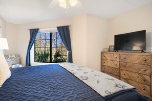 A bedroom with a bed, a television on a wooden dresser, and a window with curtains. - Beach Blessing - Short Walk to Beach and Coligny
2 bedroom, 2 bath condo (Hilton Head Island)