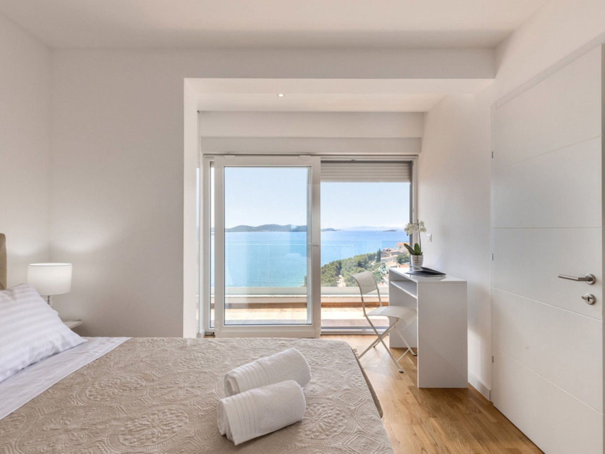 A bedroom with a bed, a desk, and a view of the sea.