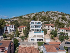 A residential area with modern houses, a central building with a swimming pool, and a hilly backdrop. - Luxury villa Fleur with pool by Interhome (Drage)
