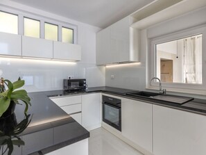 A modern kitchen with white cabinetry, a black countertop, a built-in oven, and a window with curtains. - Luxury villa Fleur with pool by Interhome (Drage)
