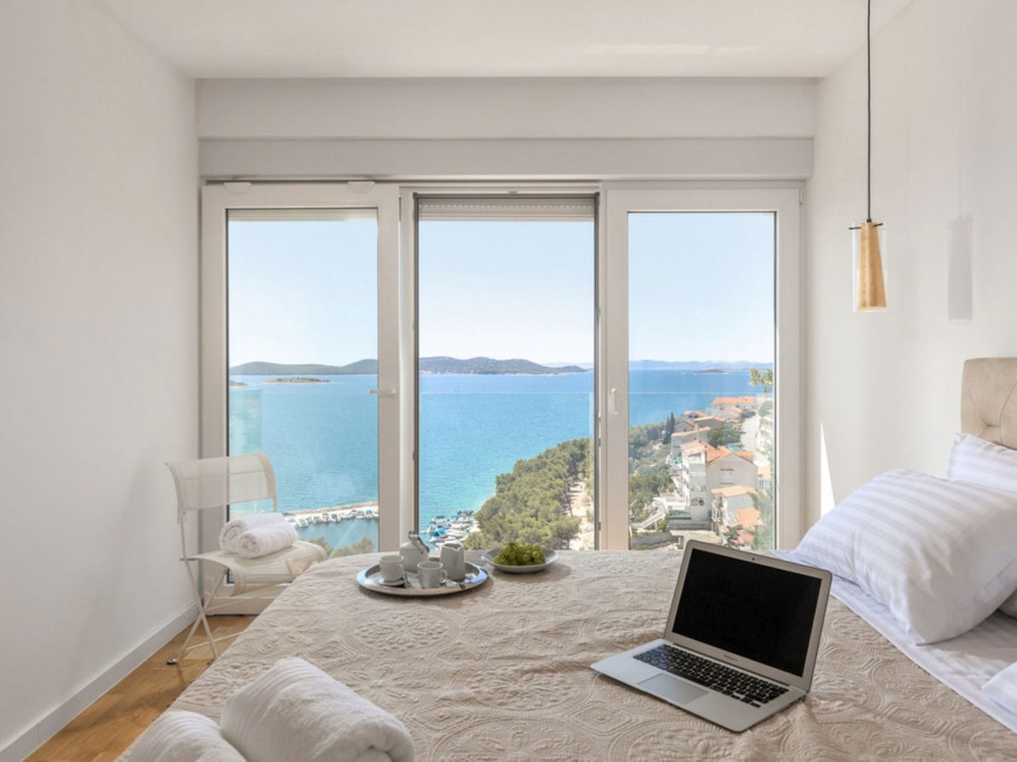A bedroom with a laptop, a bed, a chair, and a view of the sea.