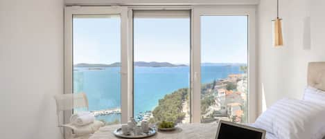 A bedroom with a laptop, a bed, a chair, and a view of the sea.