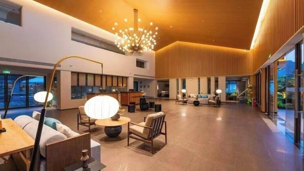 Um hall amplo com um lustre moderno, áreas de estar e grandes janelas.
