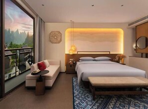 A hotel room with a bed, a sofa, a small table, a bedside table, a mirror, and a view of a mountainous landscape through large windows. - Huiting Yunju Hotel Yanshan Guilin (Guilin)