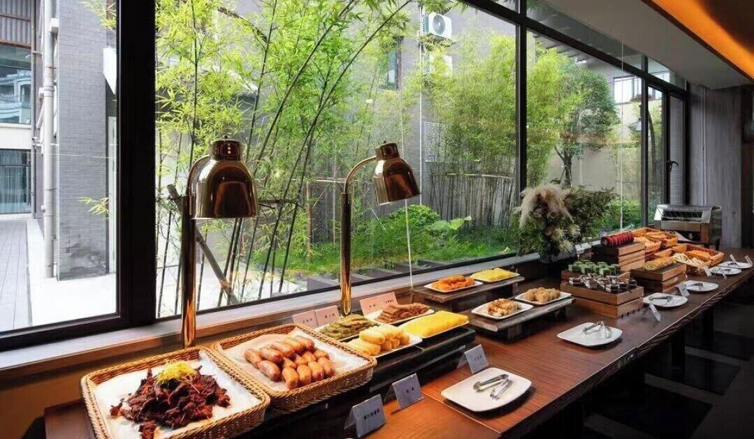 A buffet setup with various food items and a view of greenery outside.