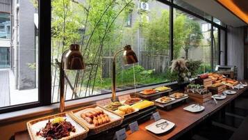 A buffet setup with various food items and a view of greenery outside.