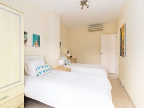 Een hotelkamer met twee bedden, een garderobe, een nachtkastje, een lamp, een airconditioner en kunst aan de muren.