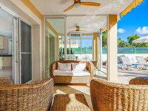 A sunlit room with wicker furniture, a ceiling fan, and a view of a pool area. - Villa Occitania by Interhome (Cala Murada)