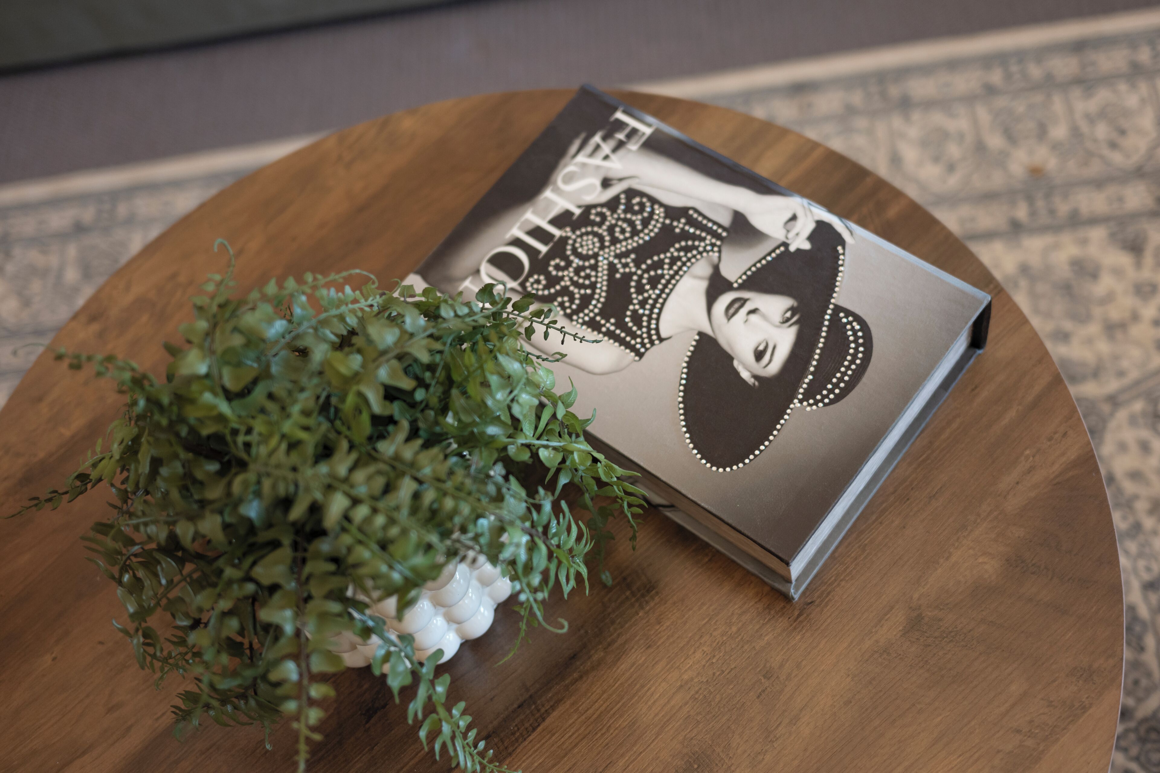 Una mesa redonda de madera con una revista que muestra un retrato de una mujer y una pequeña planta en maceta.