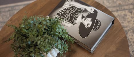 Una mesa redonda de madera con una revista que muestra un retrato de una mujer y una pequeña planta en maceta.