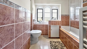A bathroom with a toilet, sink, and bathtub, featuring tiled walls and a window.