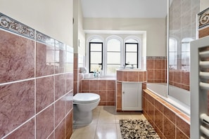 Un baño con inodoro, lavamanos y bañera, con paredes de azulejos y una ventana.