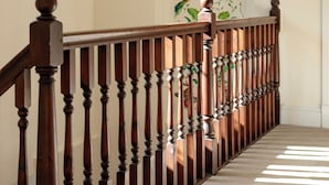 Un escalier en bois avec des balustrades, des marches recouvertes de moquette et un mur orné d’une fresque florale.